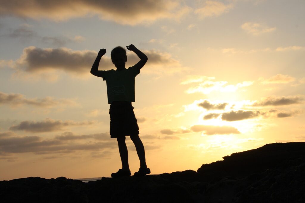 Child with arms raised in victory in sunset